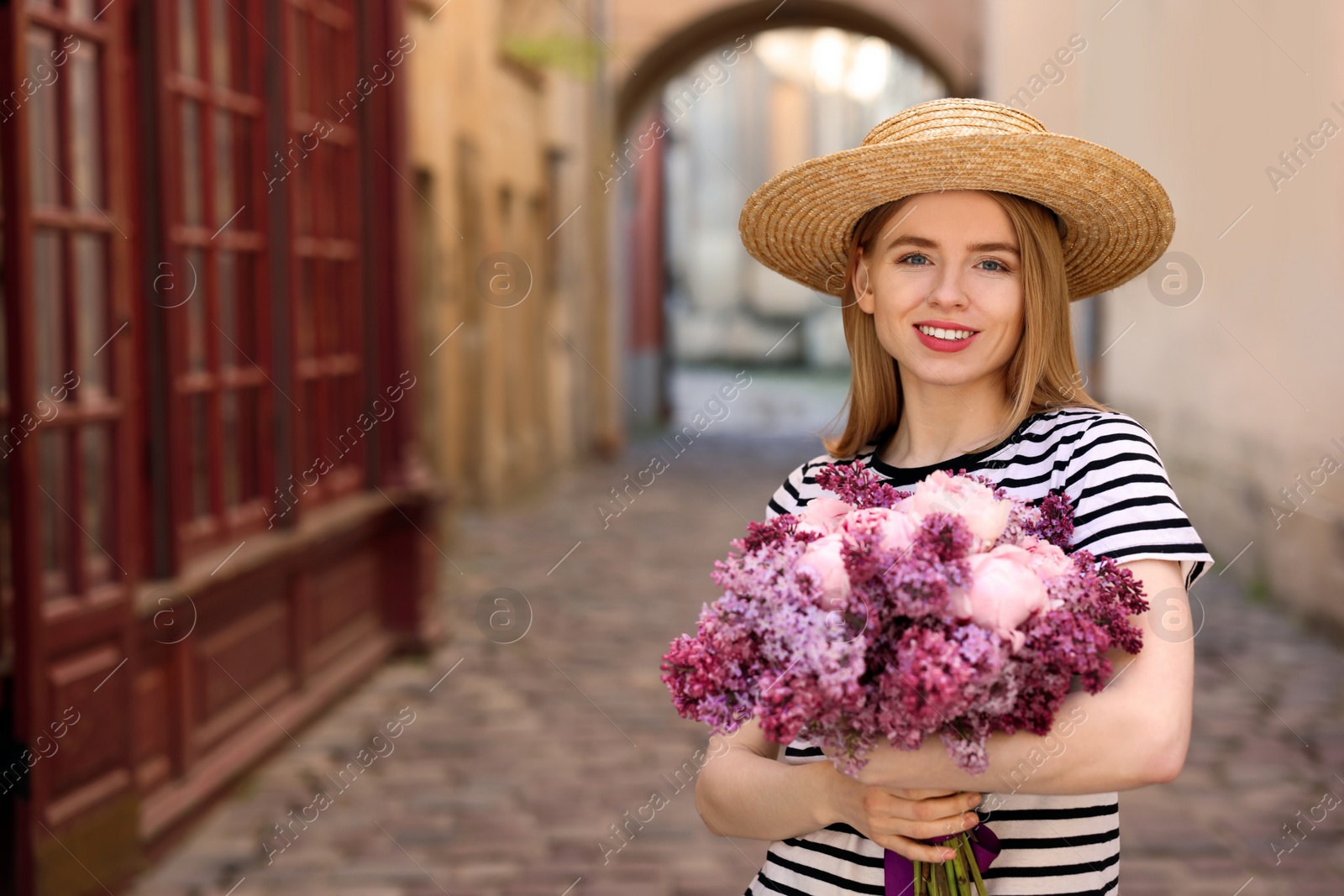 Photo of Beautiful woman with bouquet of spring flowers on city street, space for text