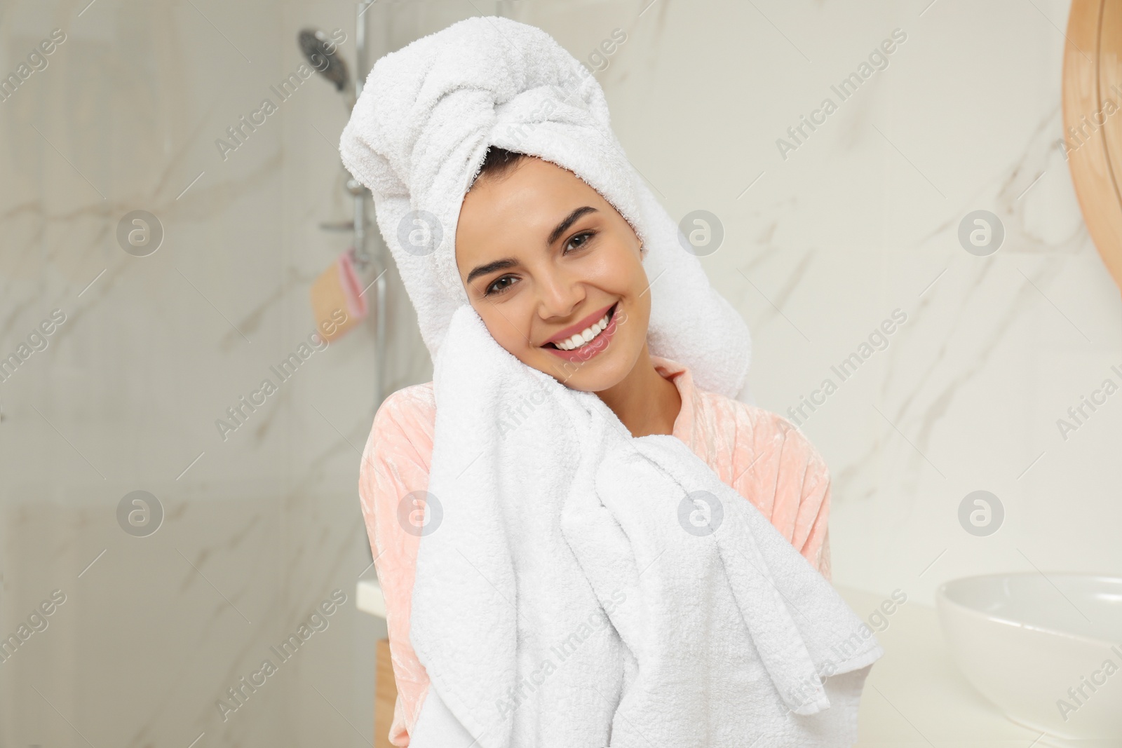 Photo of Young woman wiping face with towel in bathroom