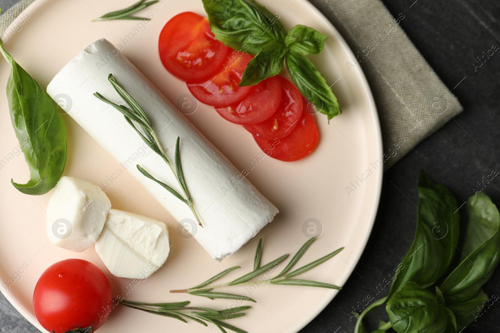 Photo of Delicious fresh goat cheese with tomatoes, basil and rosemary on grey table, flat lay