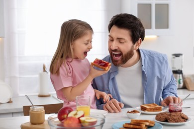 Photo of Father and his cute little daughter having fun during breakfast at table in kitchen