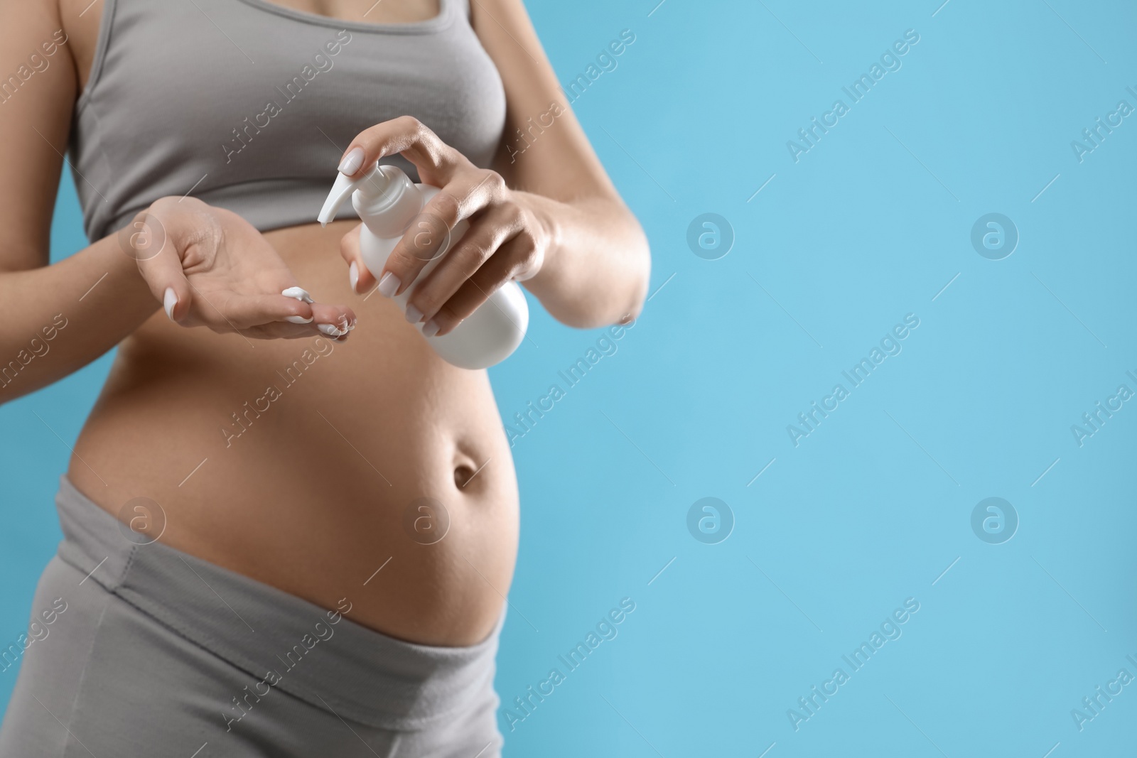 Photo of Pregnant woman with cosmetic product on light blue background, closeup. Space for text