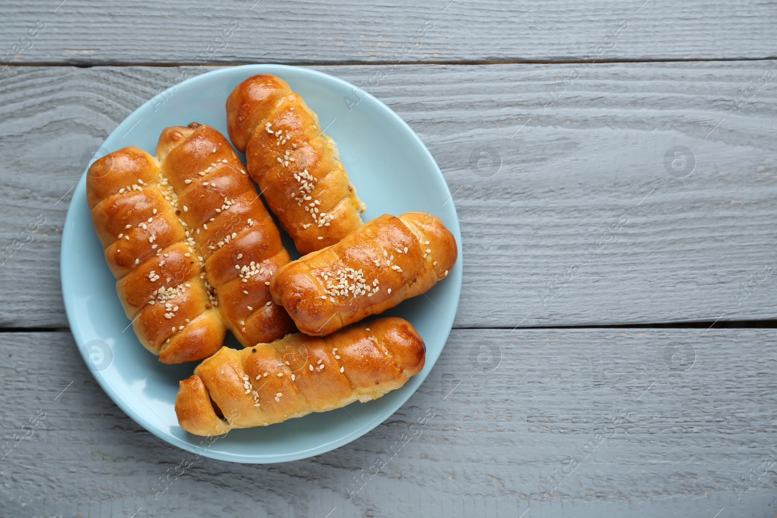 Photo of Delicious sausage rolls on grey wooden table, top view. Space for text