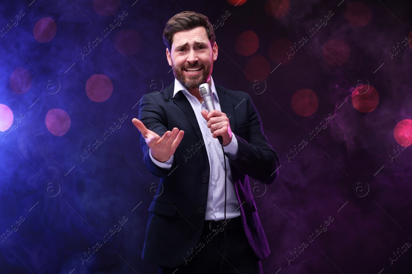 Image of Man with microphone singing on stage in color lighted smoke