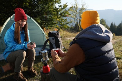 Young couple drinking coffee near camping tents in mountains