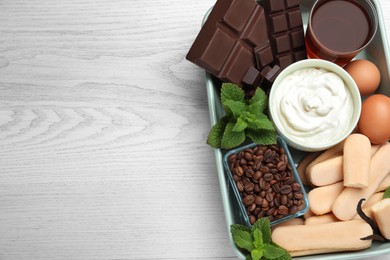 Baking dish with tiramisu ingredients on white wooden table, top view. Space for text