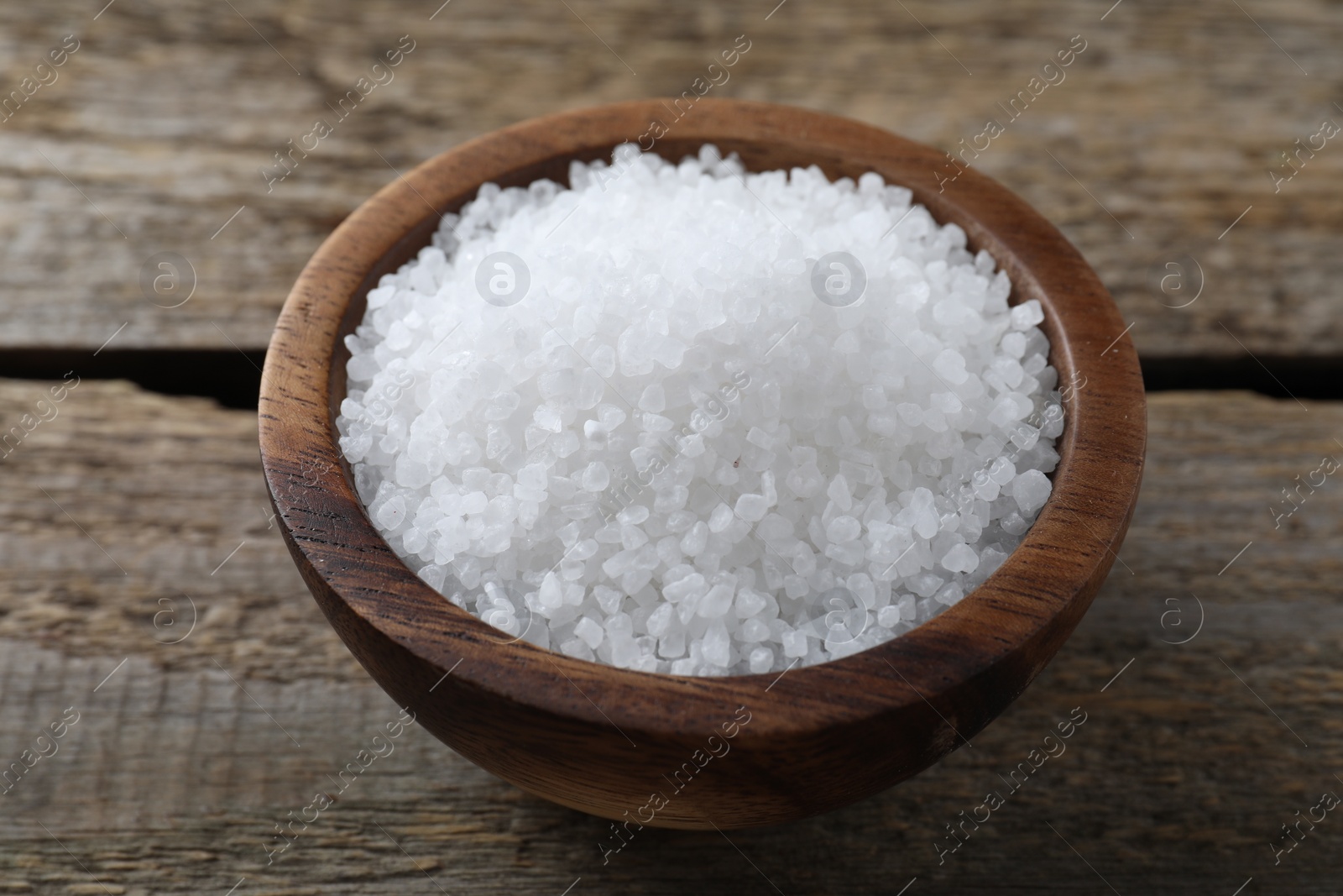 Photo of Organic salt in bowl on wooden table, closeup