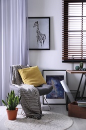 Photo of Comfortable armchair and table near window with horizontal blinds