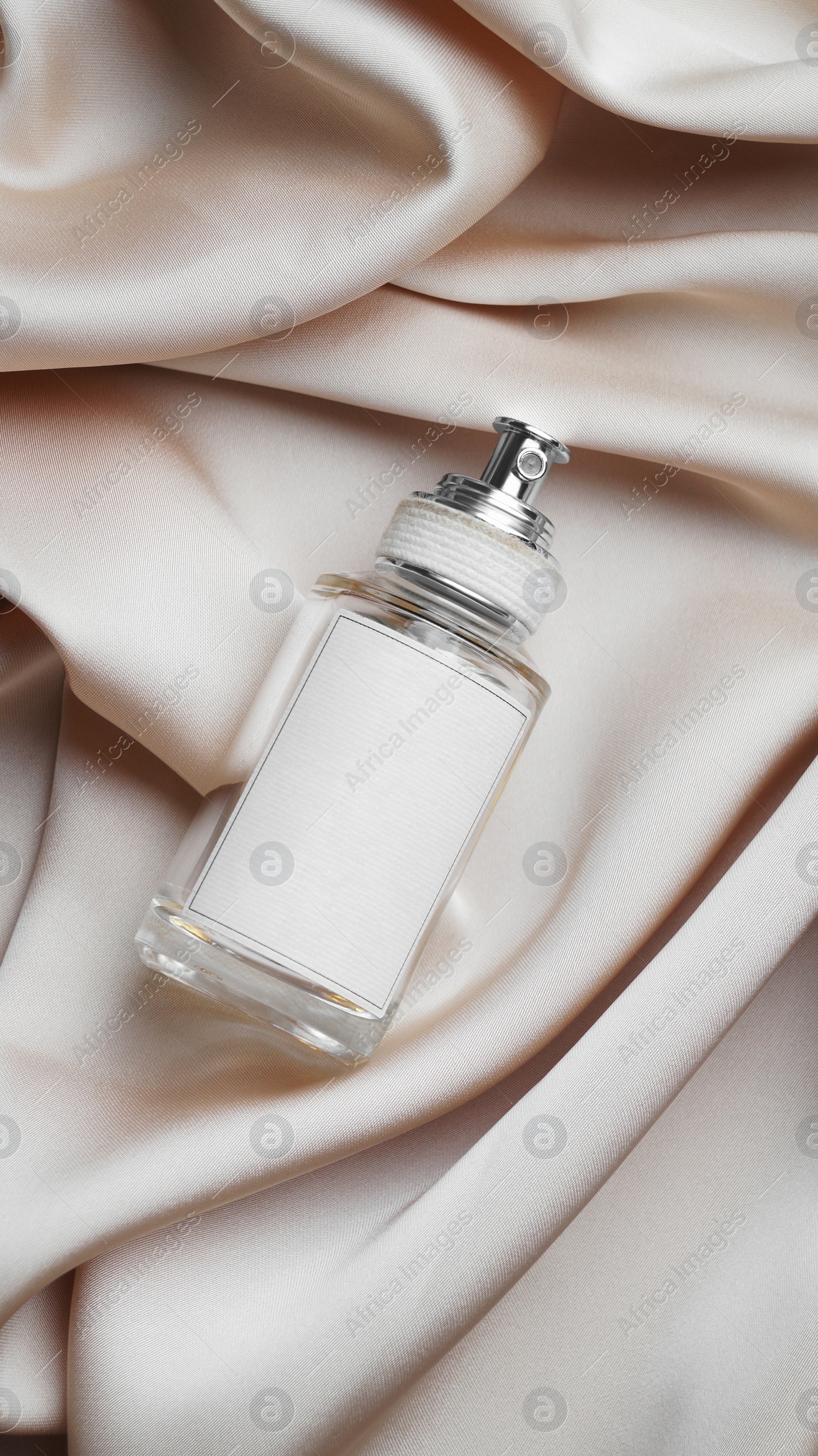 Photo of Luxury bottle of perfume on beige silk, top view