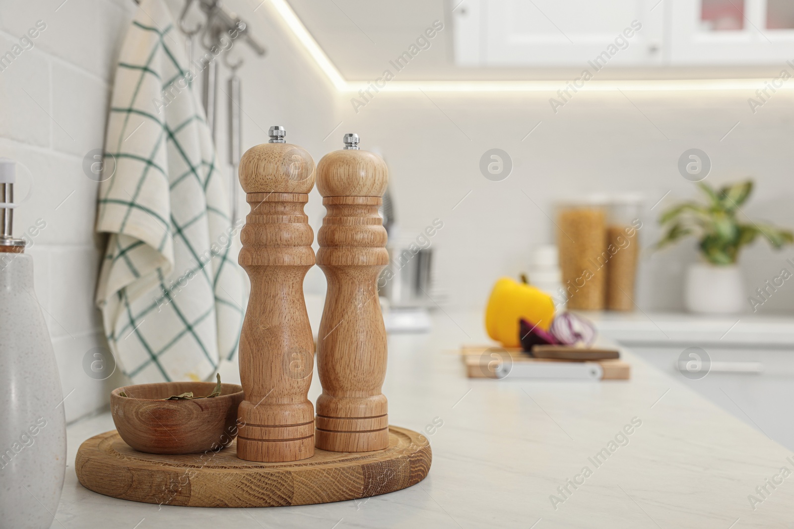 Photo of Wooden salt and pepper shakers, bowl with bay leaves on white countertop, space for text