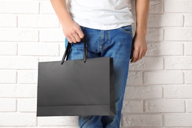 Photo of Man holding mock-up of paper shopping bag against wall