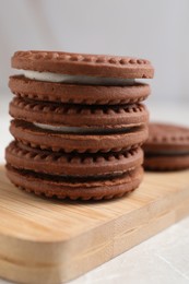Photo of Tasty chocolate sandwich cookies with cream on wooden board, closeup