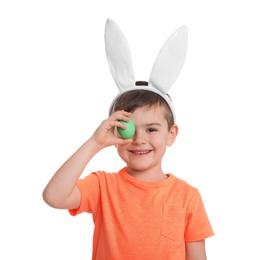 Photo of Little boy in bunny ears headband holding Easter egg near eye on white background