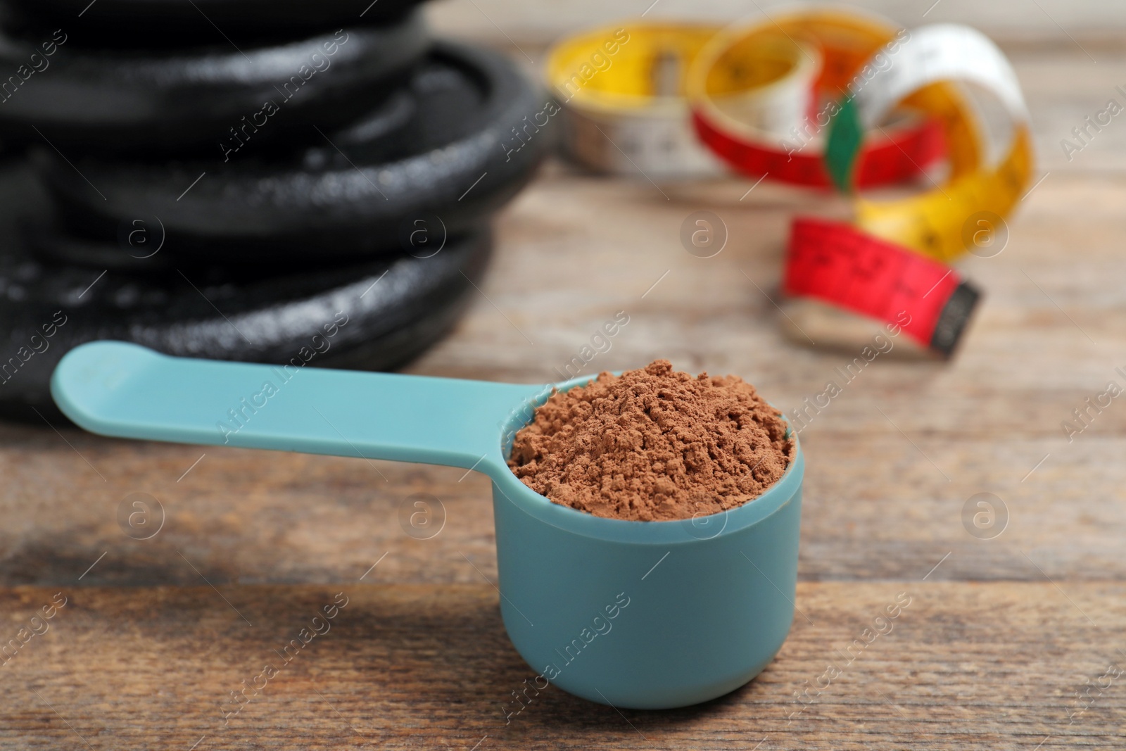 Photo of Scoop with protein powder, measuring tape and dumbbell plates on wooden table. Space for text