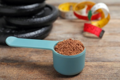 Photo of Scoop with protein powder, measuring tape and dumbbell plates on wooden table. Space for text