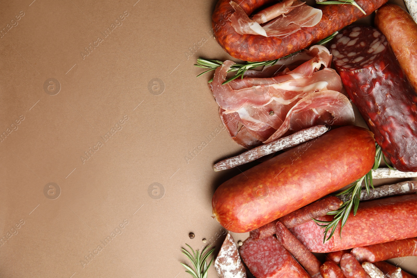 Photo of Different types of sausages with rosemary on brown background, flat lay. Space for text