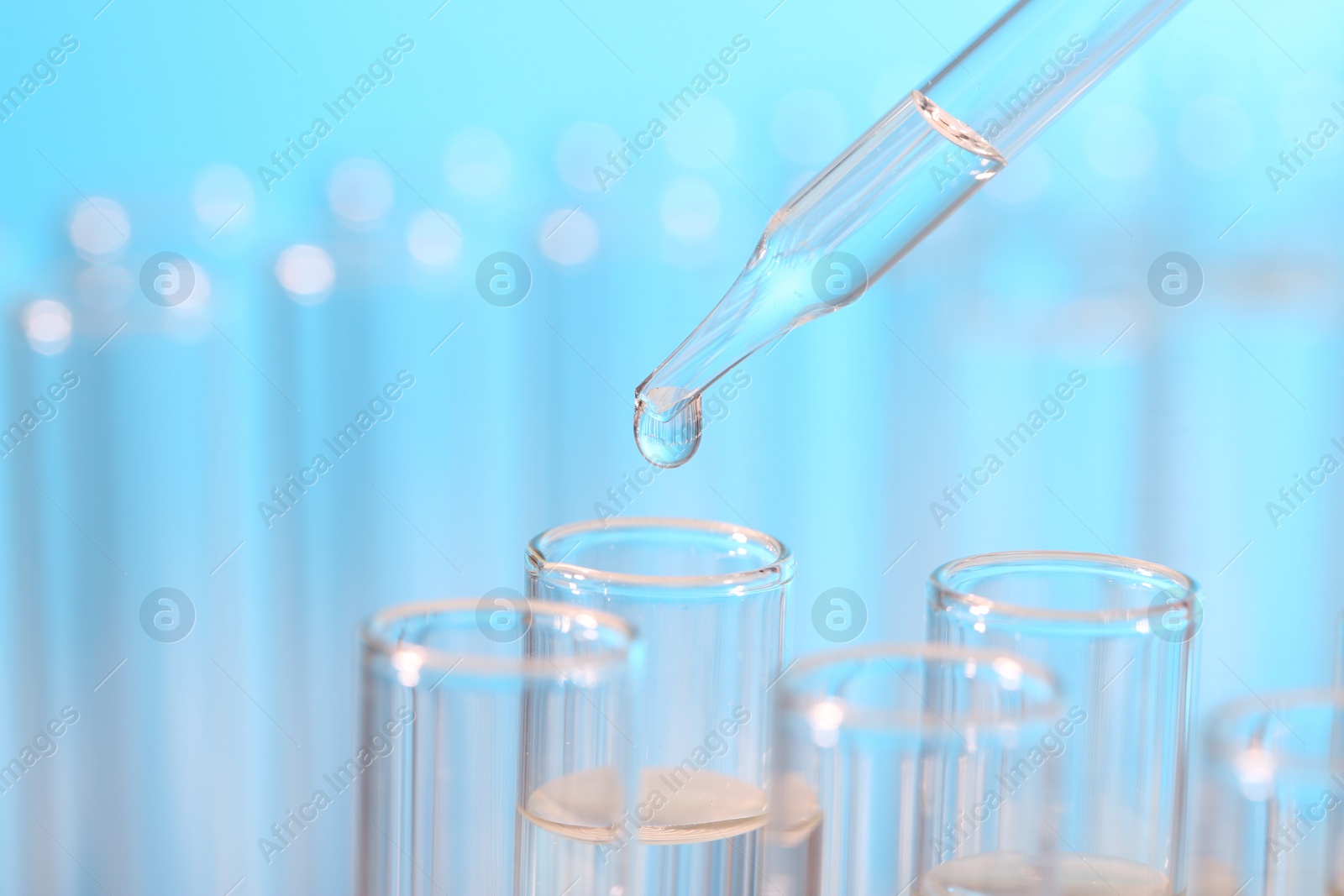 Photo of Laboratory analysis. Dripping liquid from pipette into glass test tube on light blue background, closeup and space for text