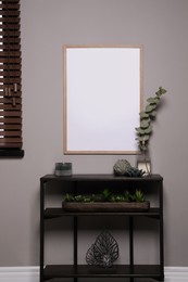 Photo of Empty frame hanging on grey wall over wooden console table with decor. Mockup for design
