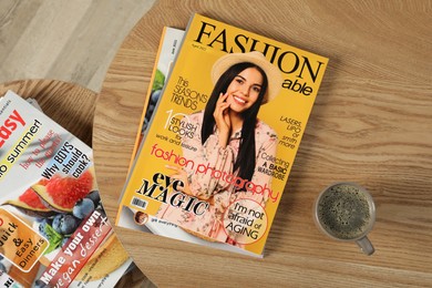 Wooden nesting tables with different magazines and cup of coffee indoors, top view