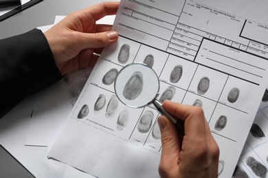 Female criminalist exploring fingerprints with magnifier at table, closeup