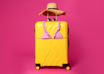 Photo of Stylish suitcase with hat, sunglasses and bikini top on color background