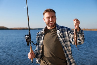 Photo of Fisherman holding fishing rod and catch at riverside