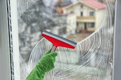 Woman cleaning window with squeegee indoors, closeup