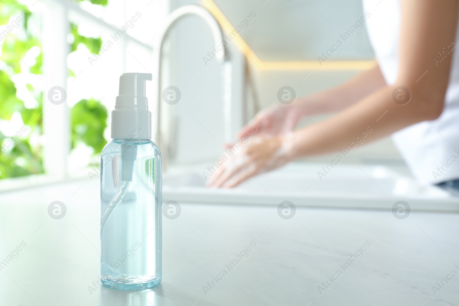 Photo of Bottle of antibacterial soap and blurred woman washing hands on background. Personal hygiene during COVID-19 pandemic