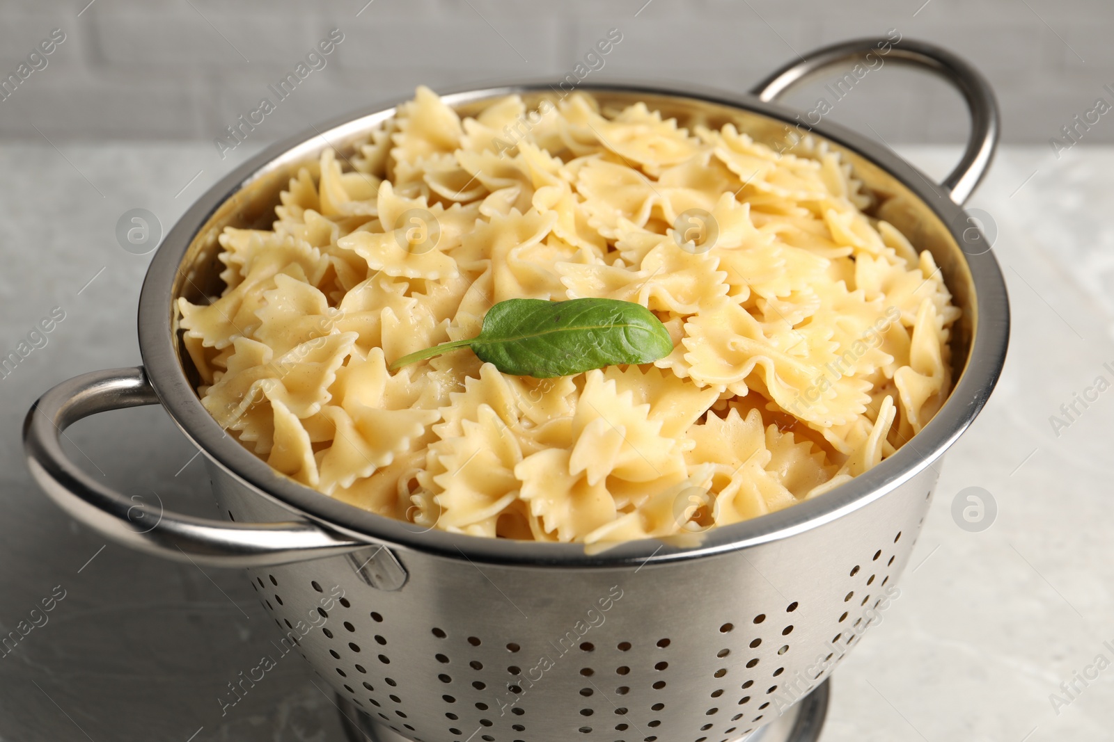 Photo of Cooked pasta in metal colander on grey table, closeup