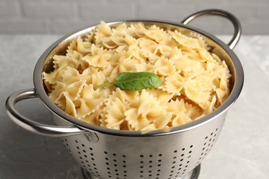 Cooked pasta in metal colander on grey table, closeup