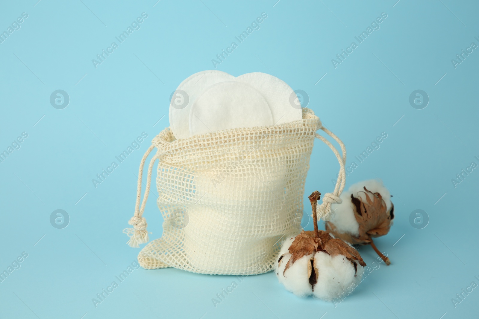 Photo of Bag with cotton pads and flowers on light blue background