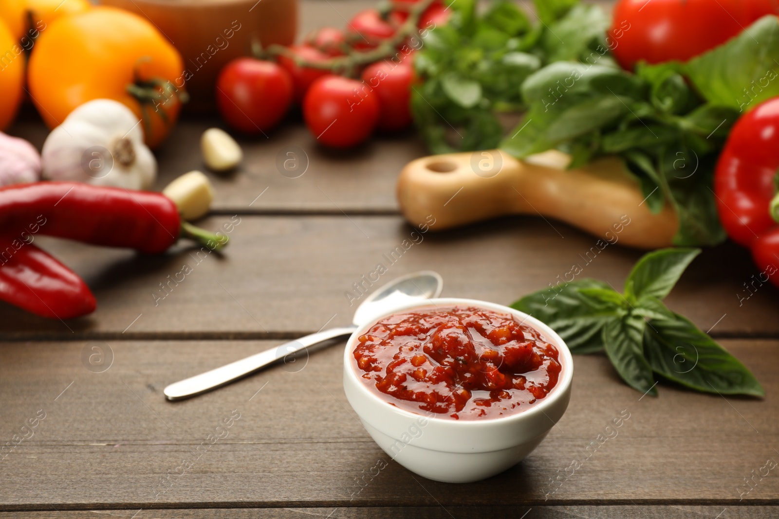 Photo of Delicious adjika sauce in bowl and ingredients on wooden table