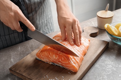 Photo of Woman cutting raw salmon fillet on wooden board