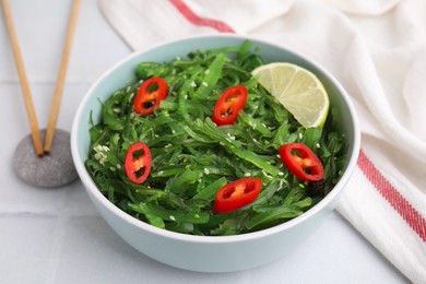 Photo of Tasty seaweed salad in bowl served on white tiled table, closeup