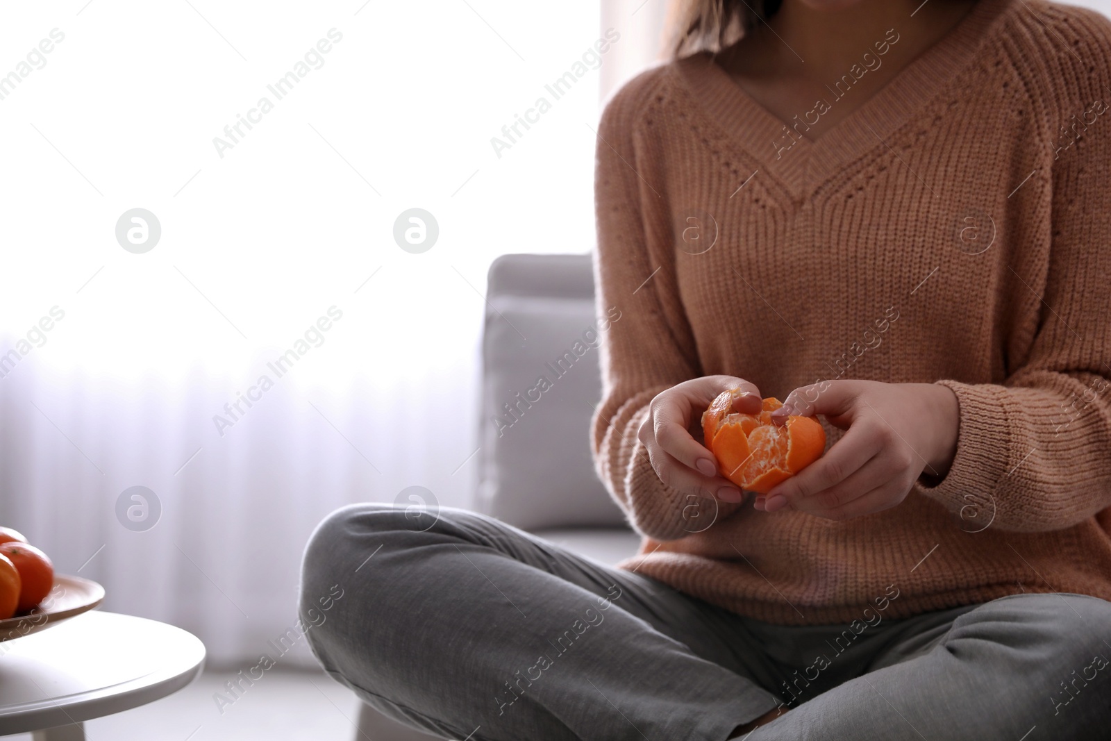 Photo of Young woman peeling fresh tangerine on sofa at home, closeup