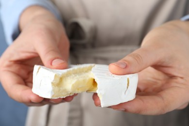 Photo of Woman breaking delicious brie cheese on color background, closeup