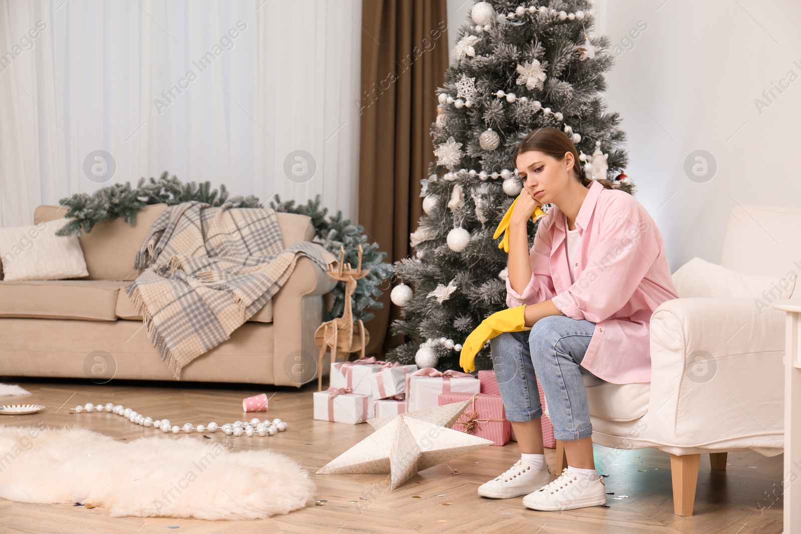 Photo of Tired woman sitting in messy room while cleaning after New Year party