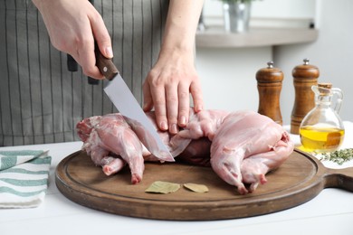 Woman cutting whole raw rabbit at white wooden table, closeup