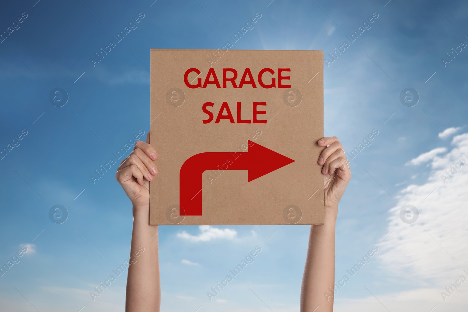 Image of Woman holding sign with text GARAGE SALE against blue sky