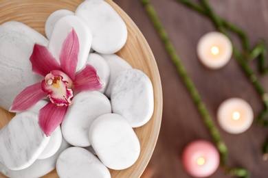 Photo of Wooden plate with spa stones and orchid flower on blurred background. Space for text