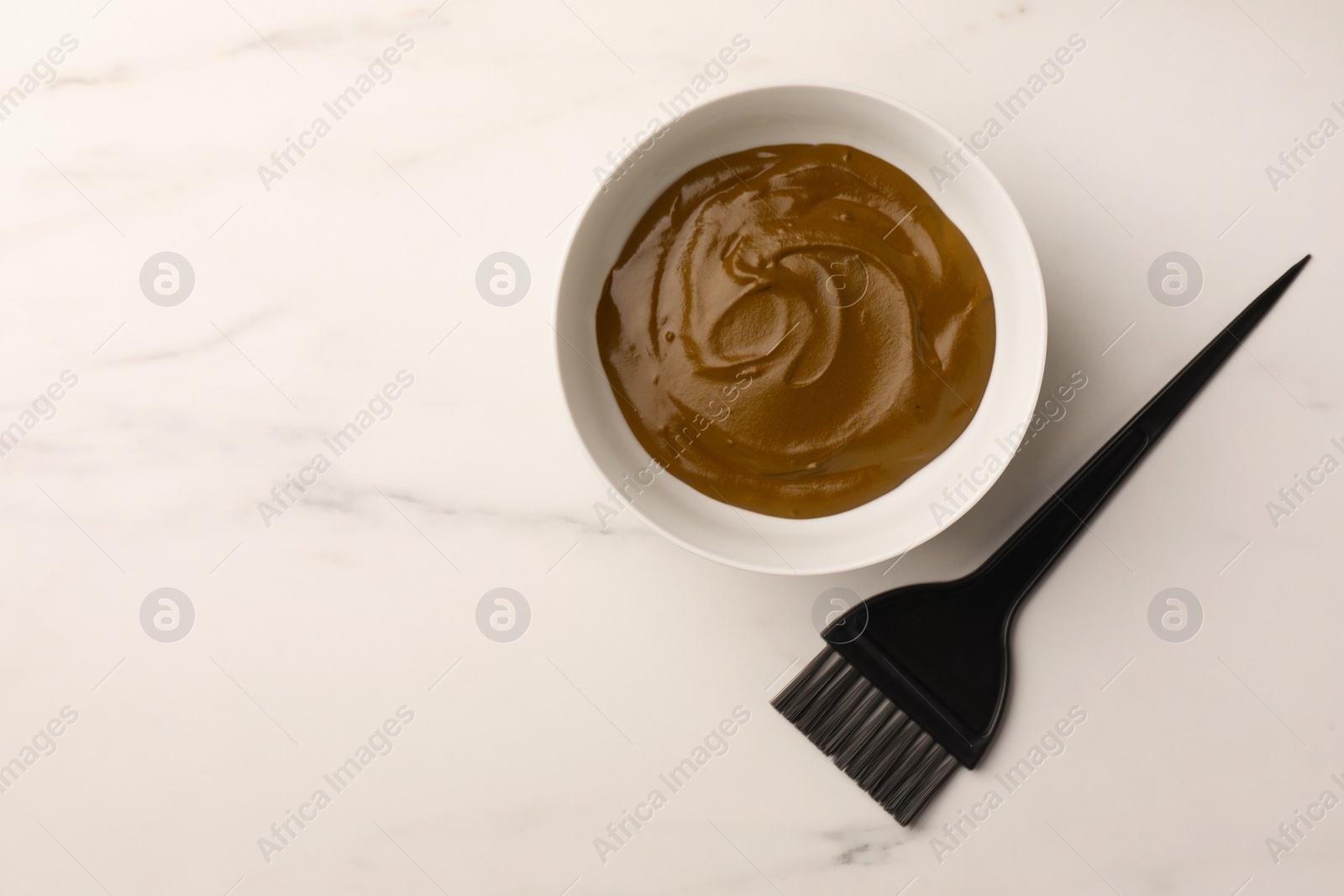 Photo of Bowl of henna cream and brush on white marble table, flat lay with space for text. Natural hair coloring