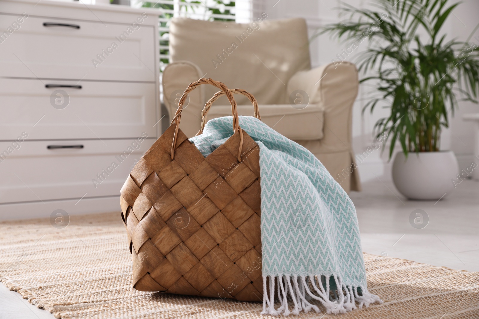 Photo of Stylish wicker basket with light blue scarf on floor indoors