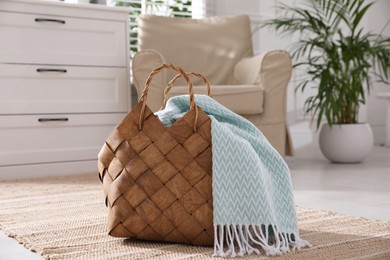 Photo of Stylish wicker basket with light blue scarf on floor indoors