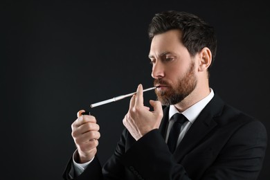 Photo of Man using long cigarette holder for smoking on black background, space for text