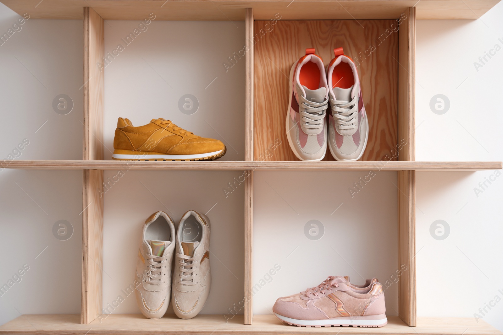 Photo of Wooden shelving unit with stylish women's sneakers on white wall