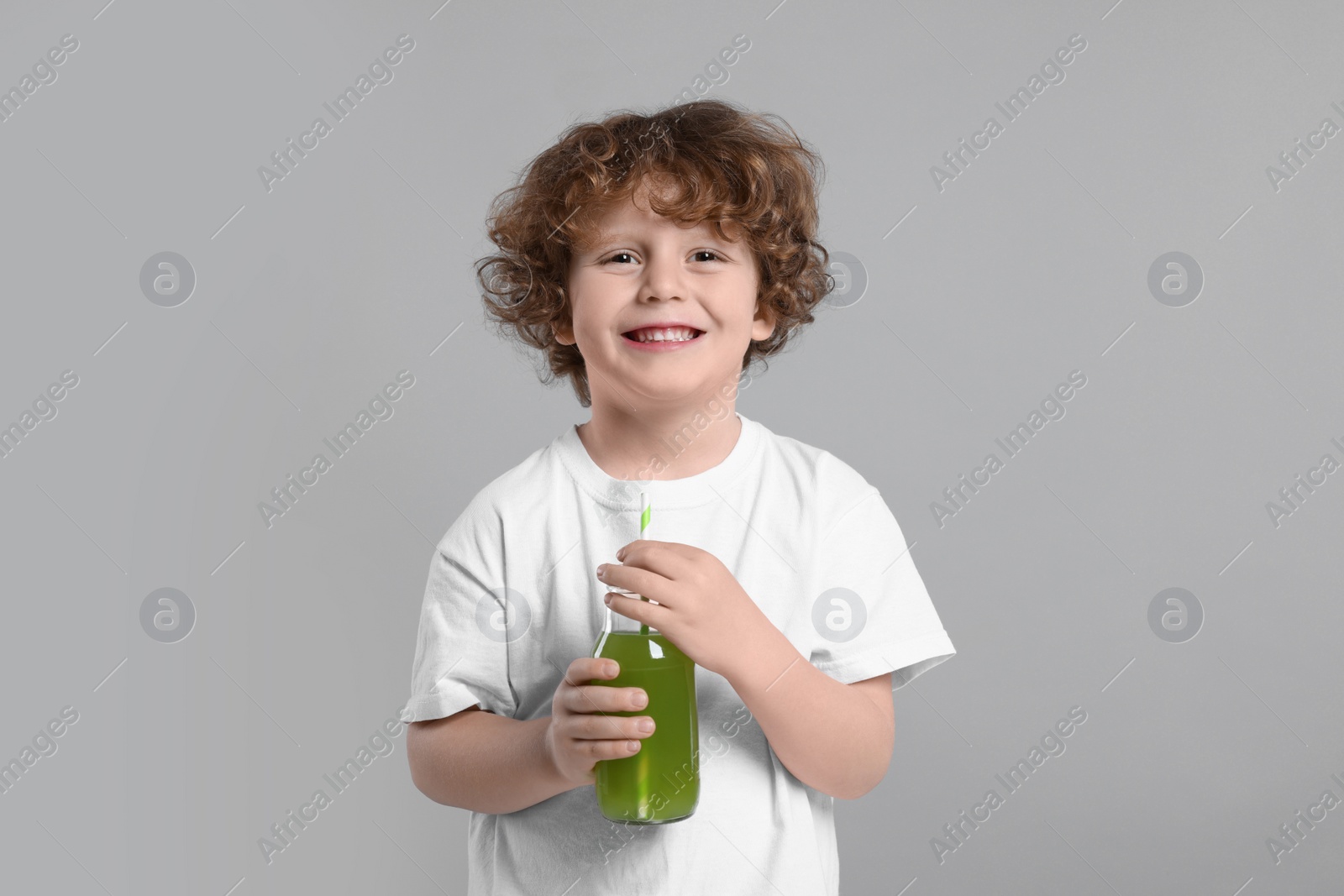 Photo of Cute little boy with glass bottle of fresh juice on light gray background