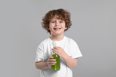 Cute little boy with glass bottle of fresh juice on light gray background