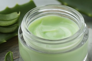 Jar with cream and cut aloe leaves on table, closeup