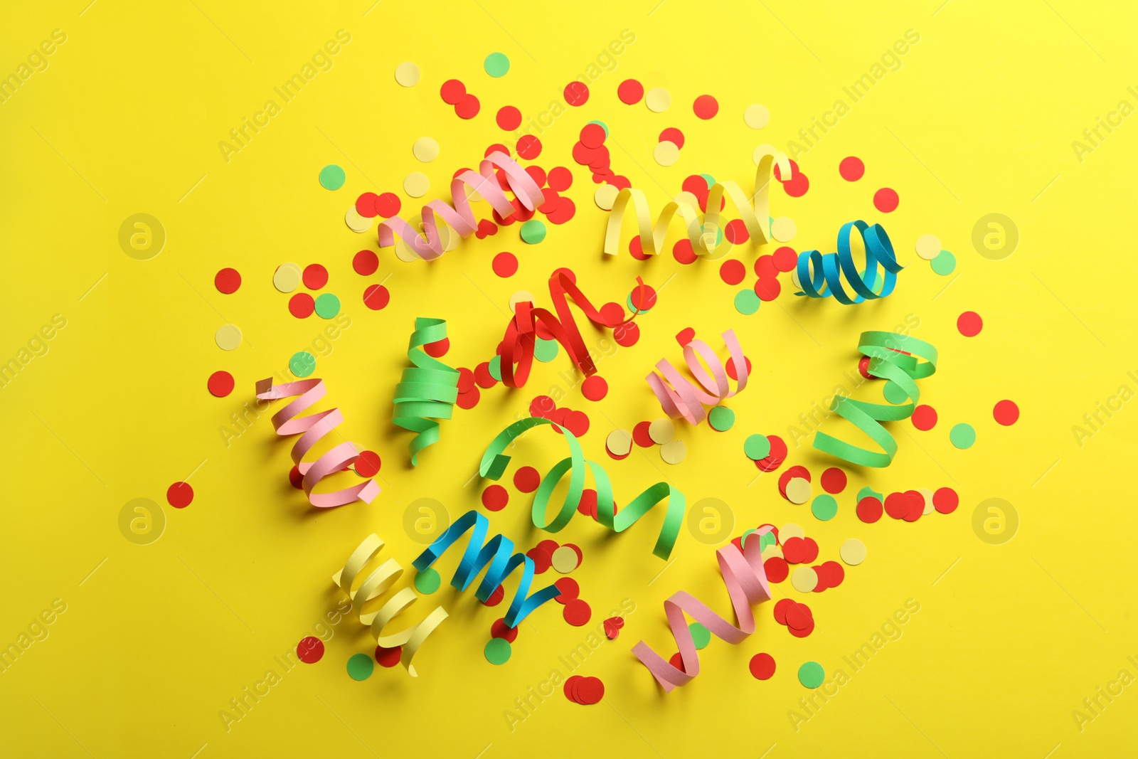 Photo of Colorful serpentine streamers and confetti on yellow background, flat lay