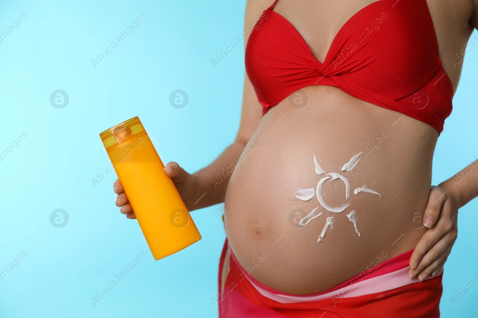 Photo of Young pregnant woman with sun protection cream on light blue background, closeup