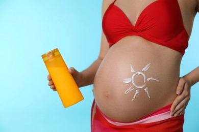 Young pregnant woman with sun protection cream on light blue background, closeup